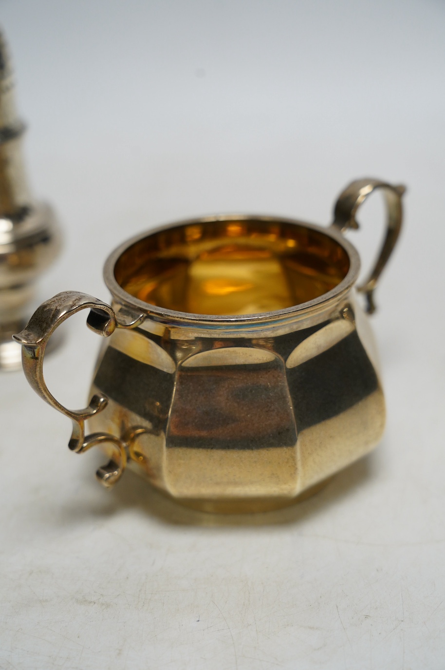 A George V silver two handled sugar bowl, Edward Barnard & Sons Ltd, London, 1926, two silver cream jugs including mounted glass and a white metal pepperette. Condition - poor to fair